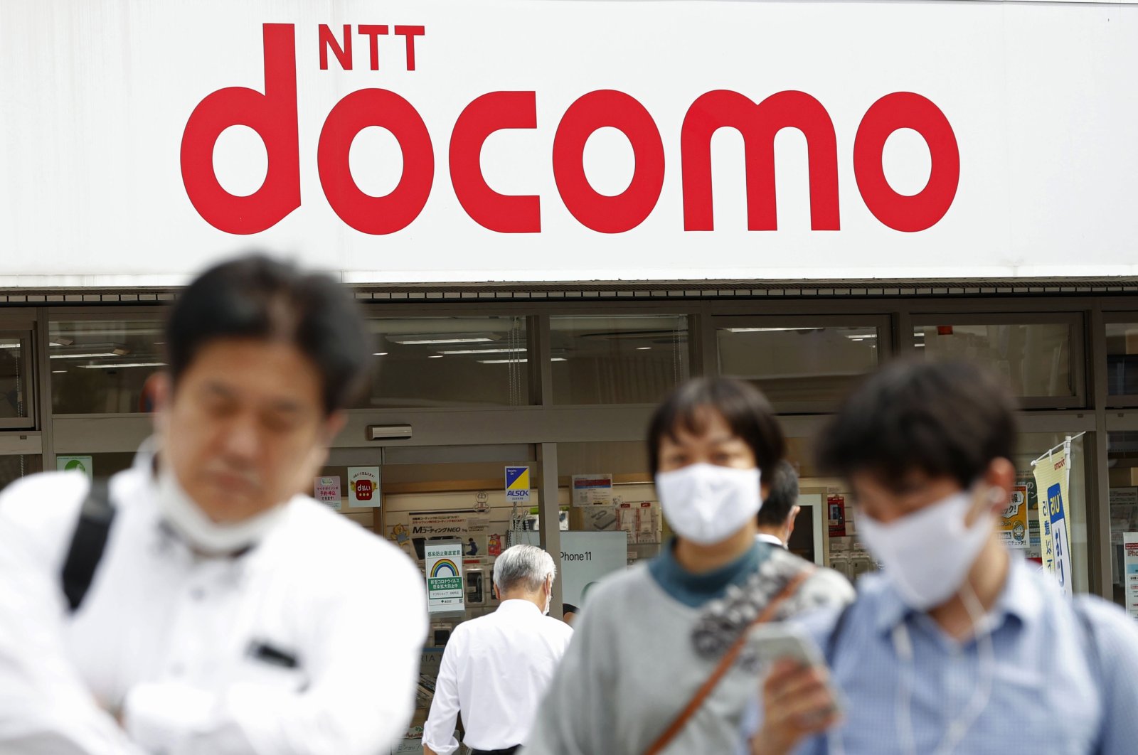 Passers-by walk past a NTT DoCoMo shop in Tokyo, Sept. 29, 2020. (AP Photo)