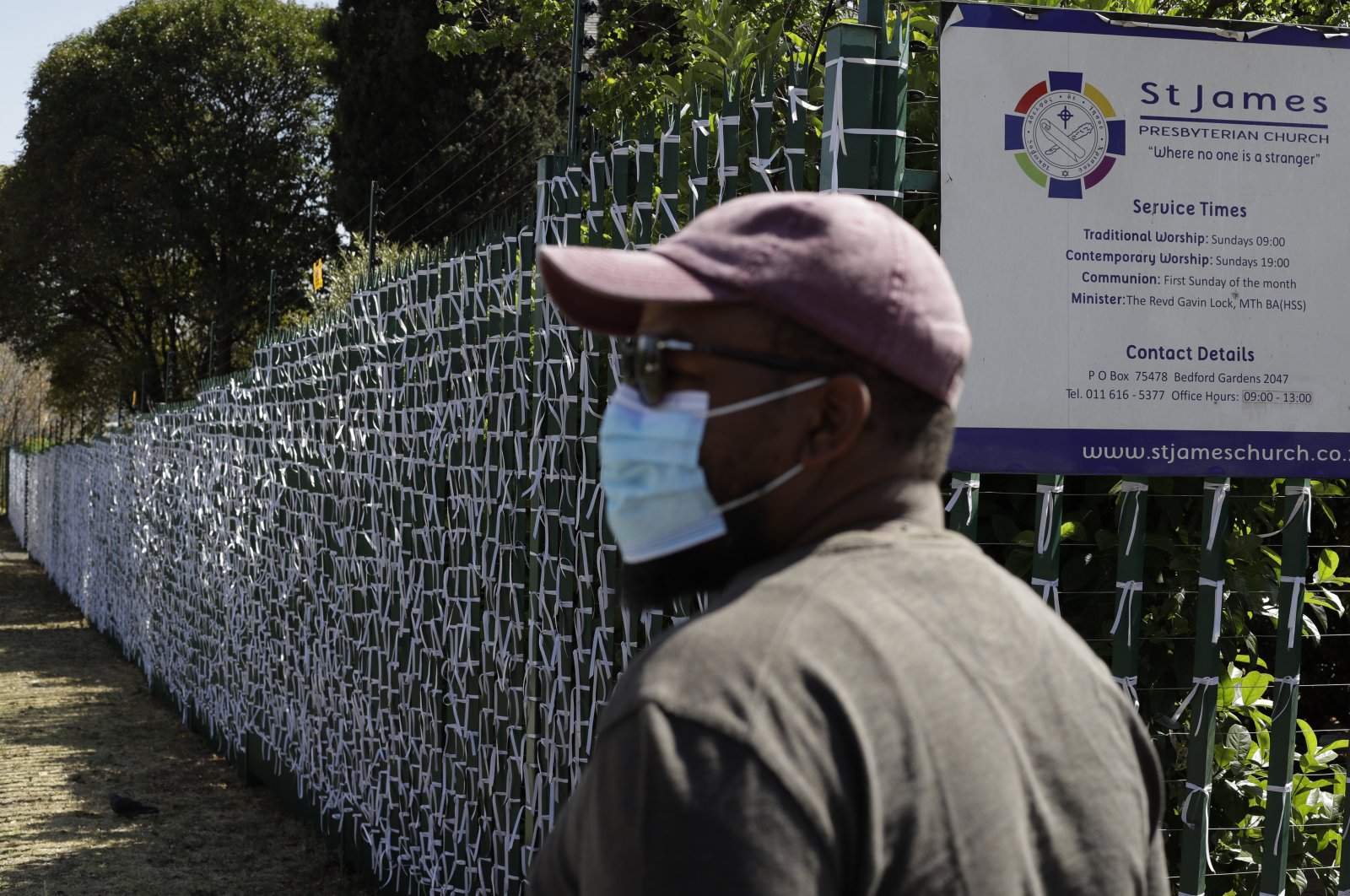 Leonard Makuya, caretaker at the St. James Presbyterian Church in Bedfordview, Johannesburg, walks past a fence with ribbons attached to represent people who have died from COVID-19 in South Africa, Sept. 29, 2020. (AP Photo)