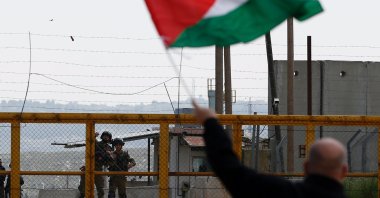 A Palestinian protester waves a national flag in front of Israeli security forces as they mark Land Day outside the compound of the Israeli-run Ofer prison near Betunia in the Israeli occupied West Bank, Palestine, March 30, 2016. (AFP Photo)