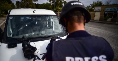 An AZTV war correspondent stands in front of their vehicle damaged in Armenian shelling in the Azerbaijani city of Tartar, Oct. 14, 2020. (IHA Photo)