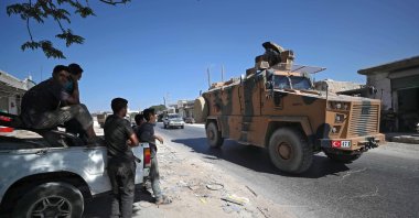 Syrians watch a Turkish military vehicle within a convoy passing through the al-Mastumah village, heading to the south of Idlib in northwestern Syria, on Oct. 14, 2020. (AFP Photo)
