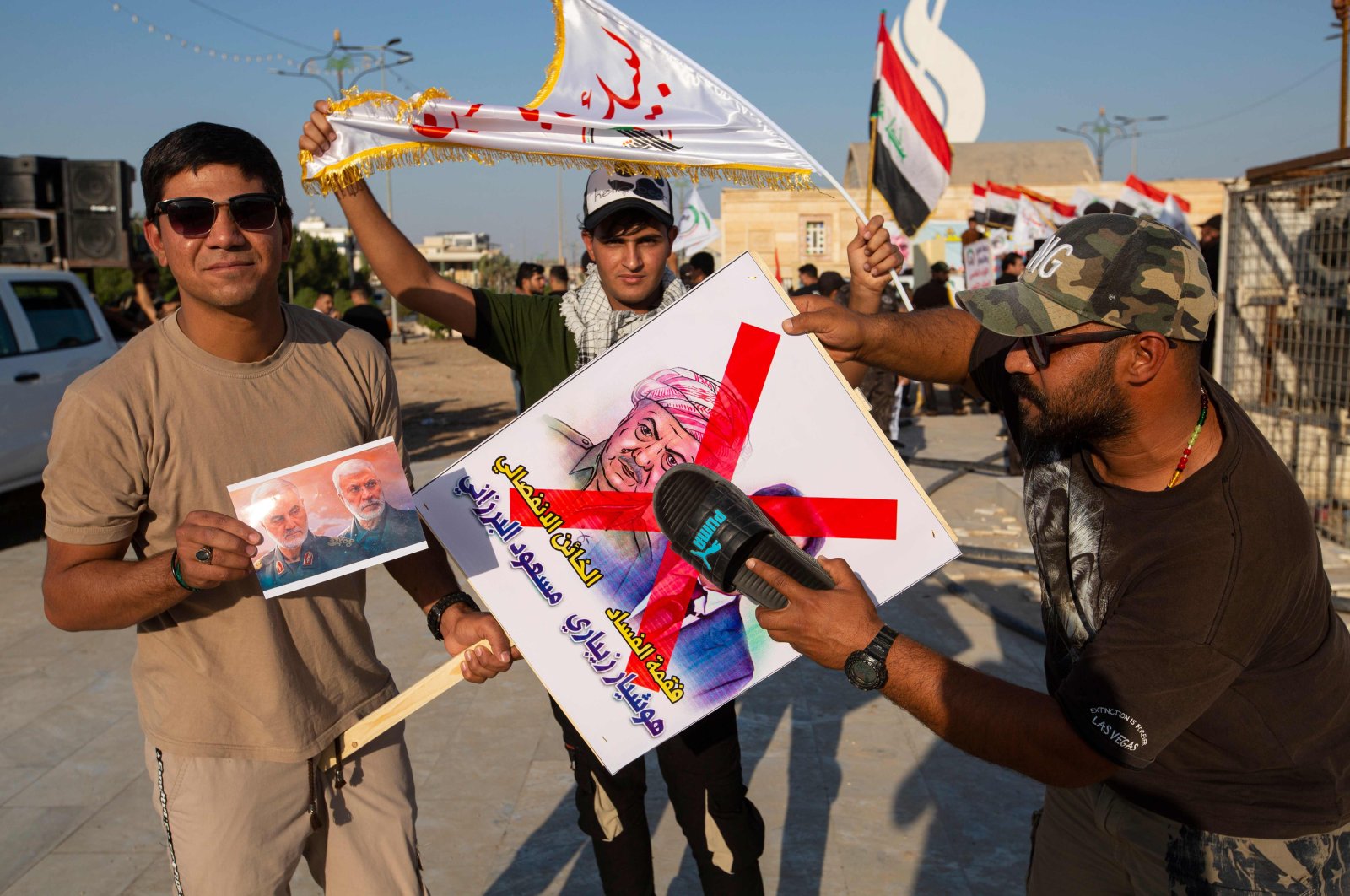 A supporter of Hashed al-Shaabi hits a poster bearing the portraits of Kurdish ex-minister Hoshyar Zebari and Kurdish leader Masoud Barzani with a slipper while a fellow protester carries the portraits of slain Iranian commander Qassem Soleimani and Iraqi paramilitary commander Abu Mahdi Al-Muhandis during a protest in support of the Hashed in the southern Iraqi city of Basra on October 17, 2020. (AFP Photo)