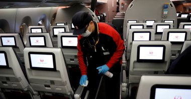 A staff member of Japan Airlines wearing a protective face mask and gloves cleans the cabin of a plane after performing a domestic flight as passengers disembarked at Haneda airport on the first day after the Japanese government lifted the state of emergency, Tokyo, Japan, May 26, 2020. (Reuters Photo)