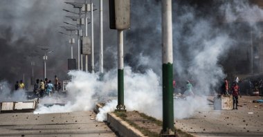 Protesters gesture and throw stones in a cloud of tear gas during a mass protest the morning after preliminary results were released for five communes in Conakry, Guinea, Oct. 21, 2020. (AFP Photo)
