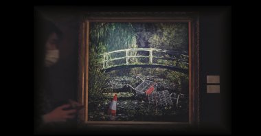 A woman walks past "Show me the Monet" by Banksy during the Sotheby's auction exhibition in Hong Kong, Oct. 3, 2020. (AP Photo)