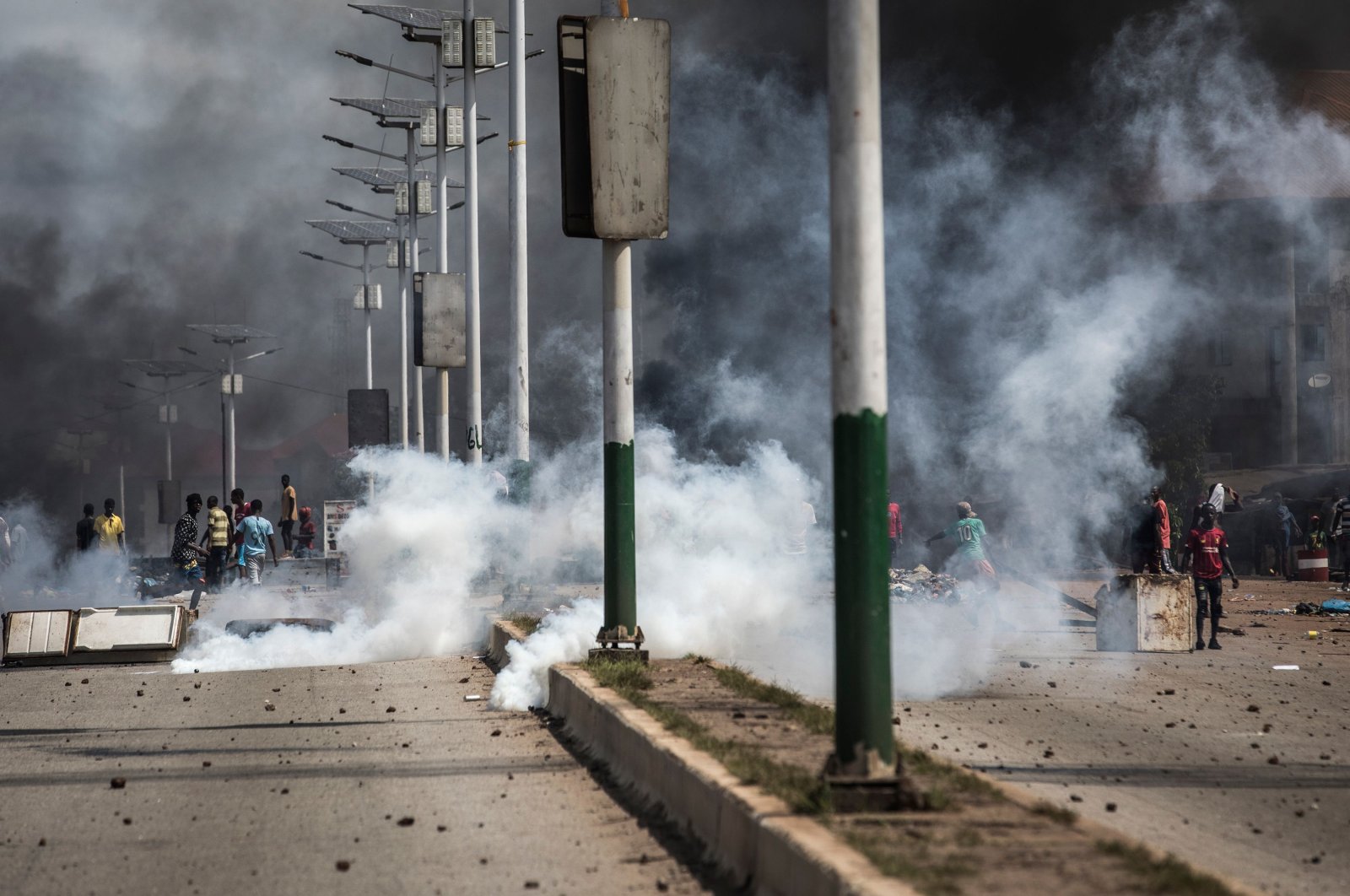 Protesters gesture and throw stones in a cloud of tear gas during a mass protest the morning after preliminary results were released for five communes in Conakry, Guinea, Oct. 21, 2020. (AFP Photo)