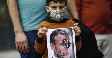 A child holds a photograph of France's President Emmanuel Macron, stamped with a shoe mark, during a protest against France in Istanbul, Oct. 25, 2020. (AP)