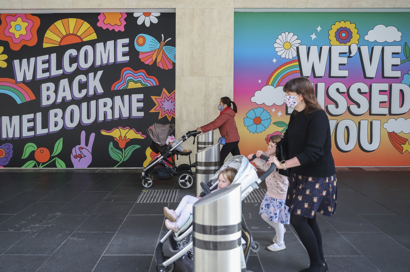 Women wearing masks push strollers past signage in Melbourne, Australia, Oct. 28, 2020. (AP Photo)