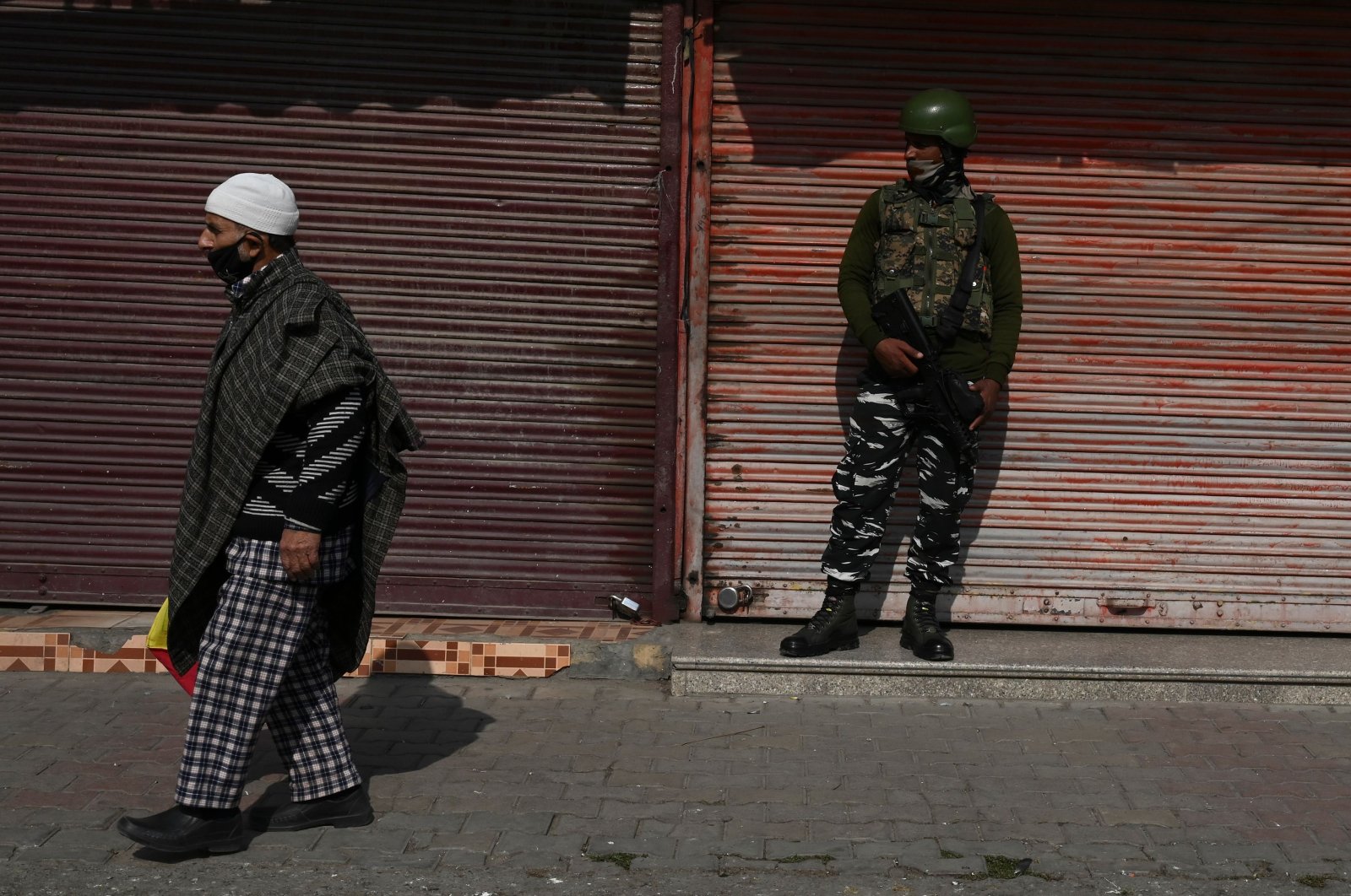 A resident walks past an Indian army soldier standing guard next to closed shops during a one-day strike called by the All Parties Hurriyat Conference (APHC) against the Indian government's decision to open Kashmir land for all Indians, in Srinagar on Oct. 31, 2020. (AFP Photo)