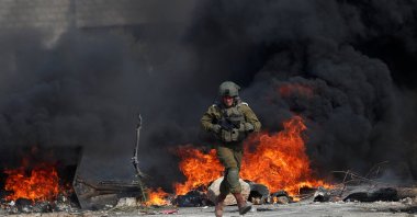 An Israeli soldier runs in front of burning tires during a Palestinian protest against Jewish settlements, in Beit Dajan in the Israeli-occupied West Bank, Oct. 30, 2020. (Reuters Photo)