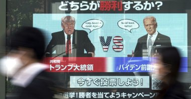 People walk past a screen showing illustrations depicting Donald Trump (L) and Joe Biden for an online vote to predict the winner in the Nov. 3 U.S. presidential election, in Tokyo on Oct. 26, 2020. (AP Photo)