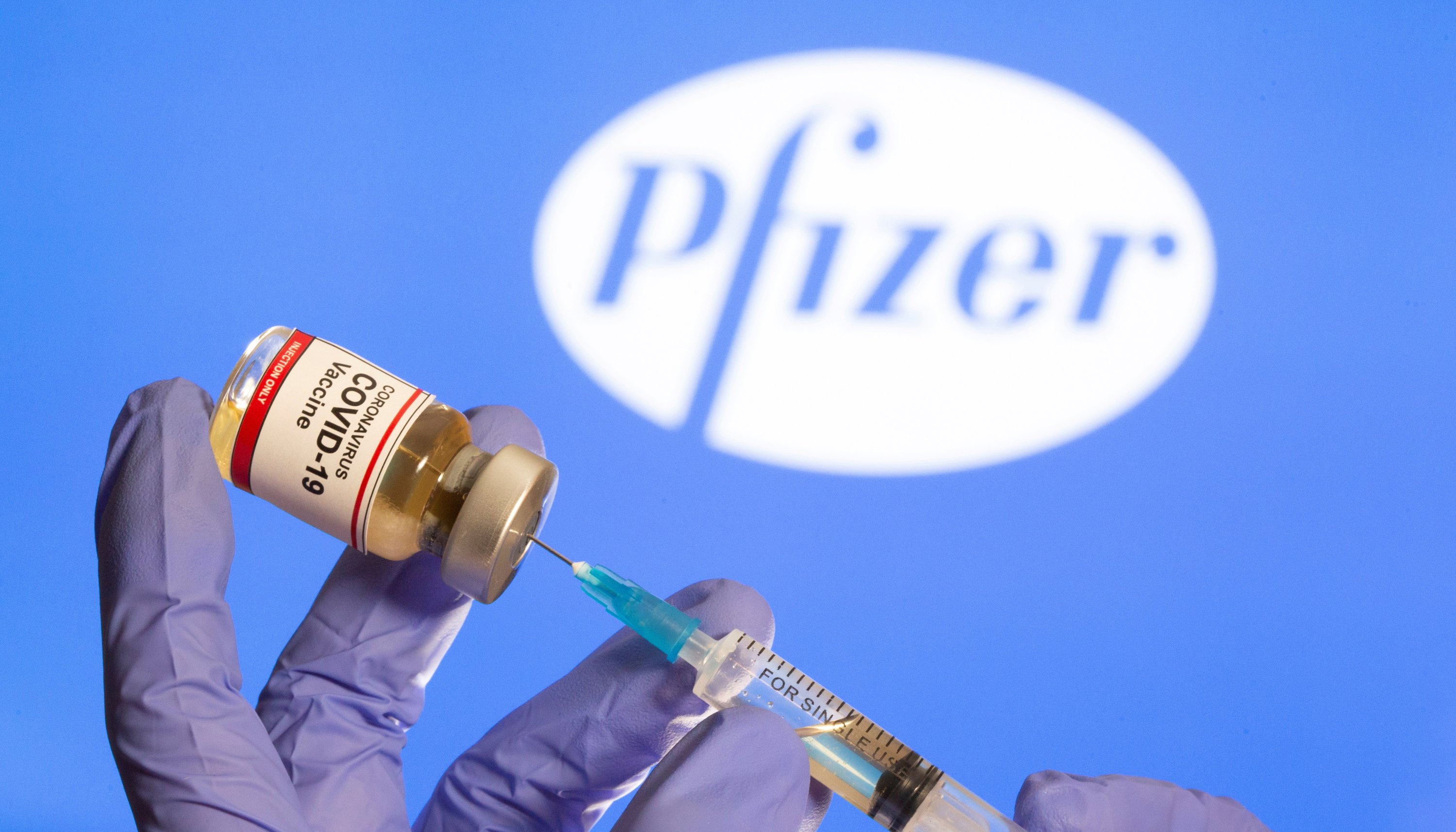 A woman holds a small bottle labeled with a 'Coronavirus COVID-19 Vaccine' sticker and a medical syringe in front of a displayed Pfizer logo, Oct. 30, 2020. (Reuters Photo)