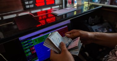 A currency exchange office worker counts Turkish lira banknotes in front of the electronic panel displaying currency exchange rates at an exchange office in Istanbul, Aug. 6, 2020. (AFP Photo)