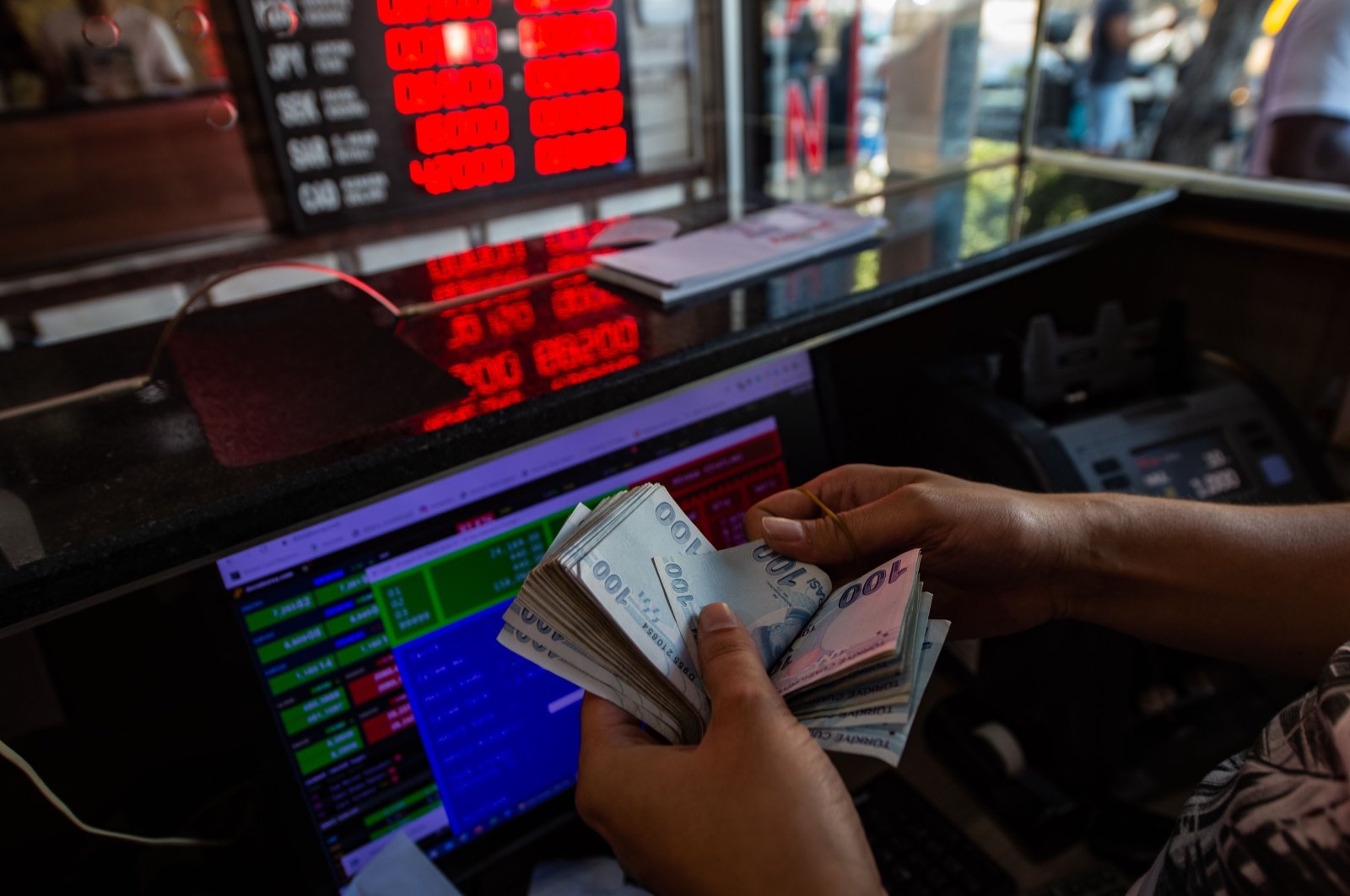 A currency exchange office worker counts Turkish lira banknotes in front of the electronic panel displaying currency exchange rates at an exchange office in Istanbul, Aug. 6, 2020. (AFP Photo)
