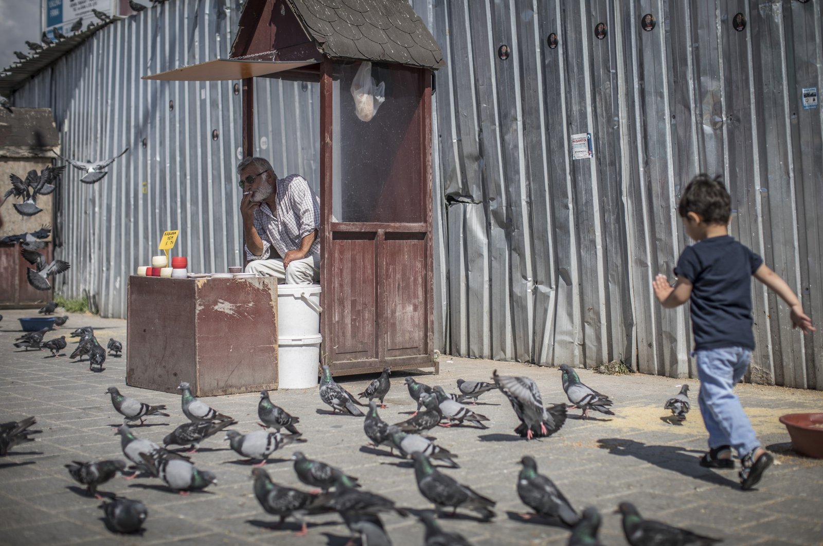 A vendor selling bird food smokes a cigarette as a boy chases pigeons in Istanbul, Turkey, 20 June 2018. (Getty Images)