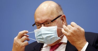 German Economy Minister Peter Altmaier takes off his mask as he arrives at a news conference to present the federal government's autumn economic forecast in Berlin, Germany, Oct. 30, 2020. (AP Photo)