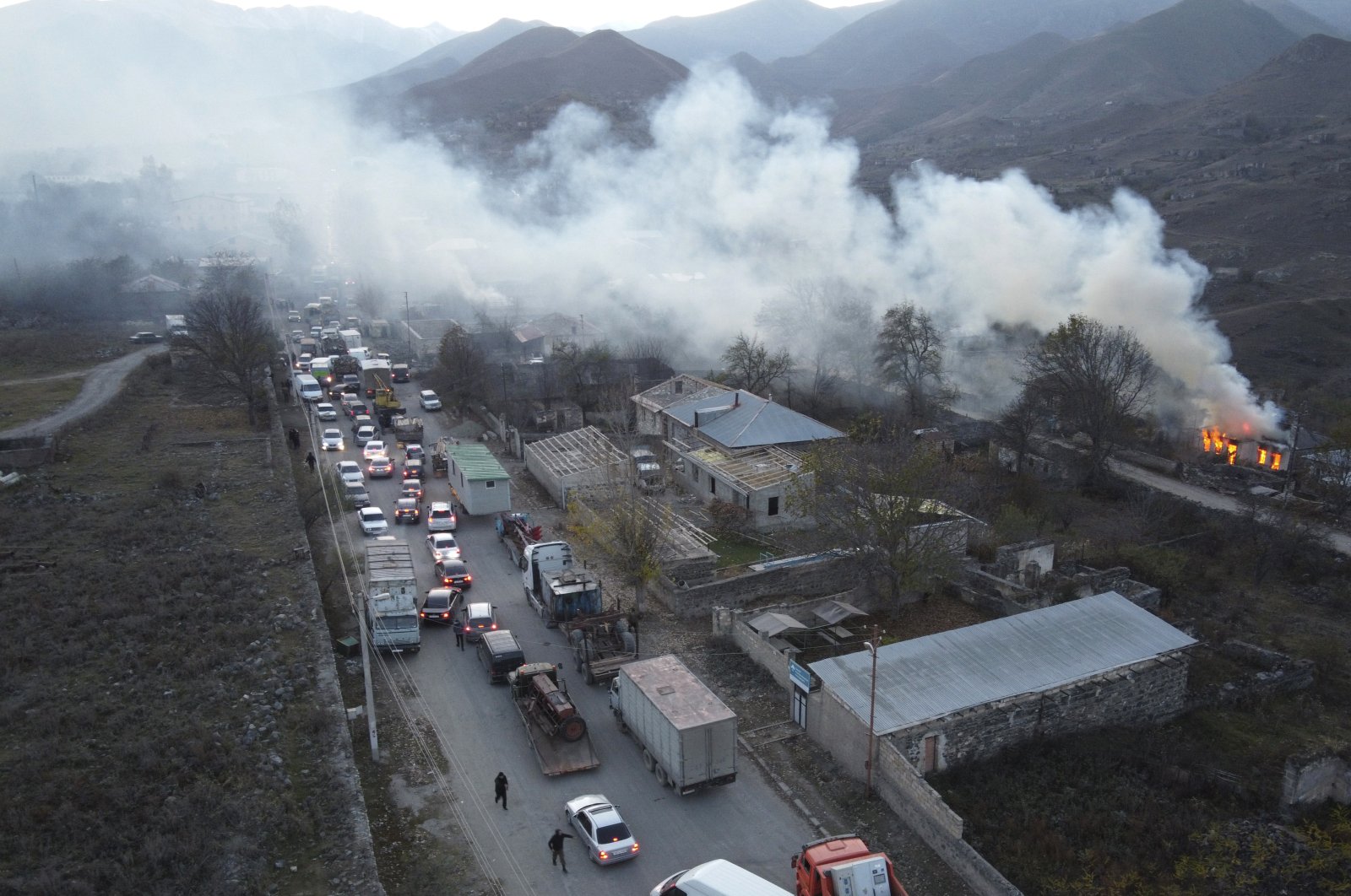 Smoke rises from a burning house as cars and trucks stuck in a traffic jam climbing along the road from Kalbajar leaving the region of Nagorno-Karabakh to Armenia, Nov. 14, 2020. (AP Photo)