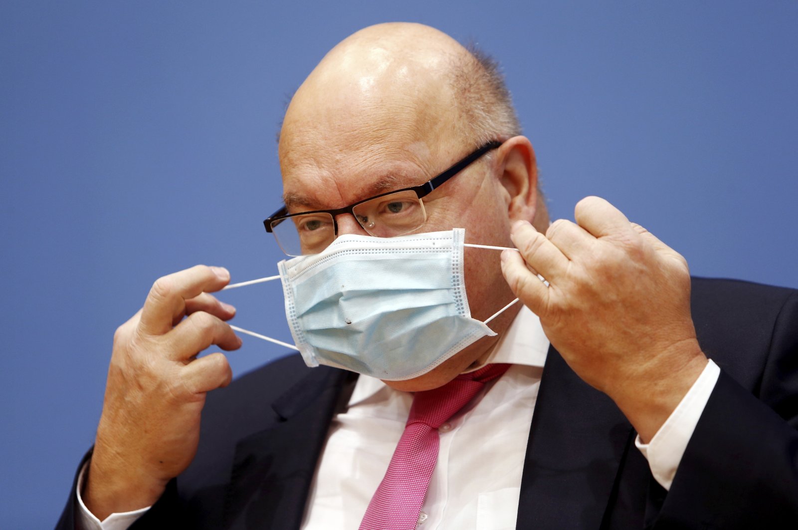 German Economy Minister Peter Altmaier takes off his mask as he arrives at a news conference to present the federal government's autumn economic forecast in Berlin, Germany, Oct. 30, 2020. (AP Photo)
