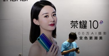 A staff member uses his smartphone in front of a billboard for Chinese smartphone brand Honor at the Global Mobile Internet Conference in Beijing, China, April 26, 2018. (AP Photo)