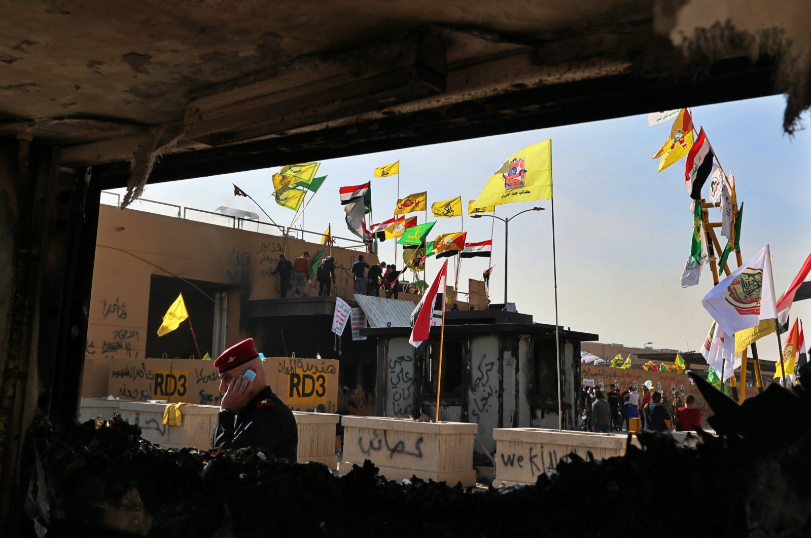 Pro-Iranian militiamen and their supporters are seen through a broken window of a burned checkpoint in front of the U.S. embassy in Baghdad, Iraq, Jan. 1, 2020. (AP Photo)