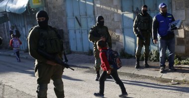 Palestinian children walk past Israeli soldiers on their way to school in the occupied West Bank city of Hebron, Feb. 12, 2019. (AP Photo)