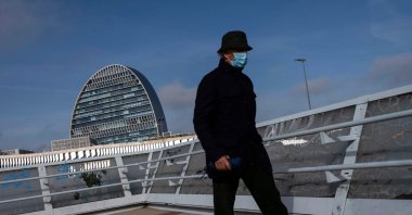 A man wearing a mask walks with La Vela (The Sail) building in the background, housing the head office of Spanish bank BBVA (Bilbao Vizcaya Argentaria Bank) in Madrid, Nov. 16, 2020. (AFP Photo)