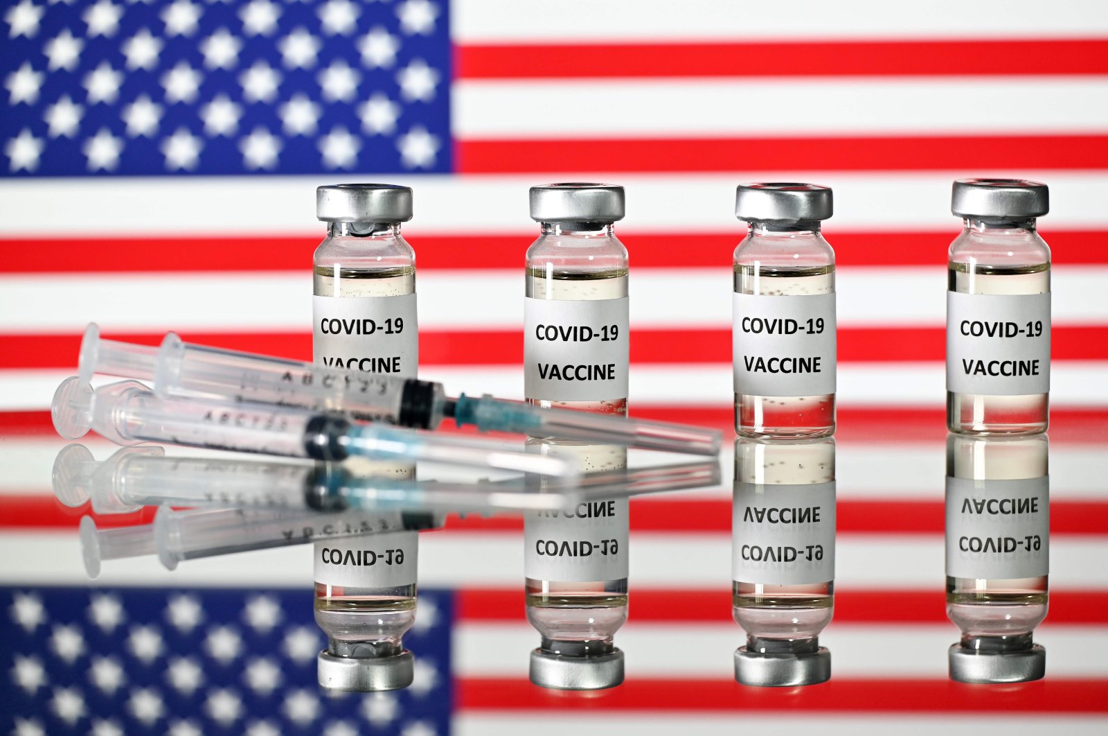 An illustration of vials with COVID-19 vaccine stickers and syringes displayed in front of the U.S. flag, Nov. 17, 2020. (AFP Photo)