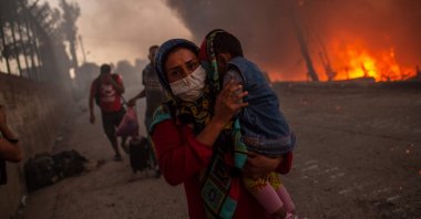 A woman carries a child past flames after a major fire broke out in the Moria migrants camp on the Aegean island of Lesbos, Greece, Sept. 9, 2020. (AFP Photo)