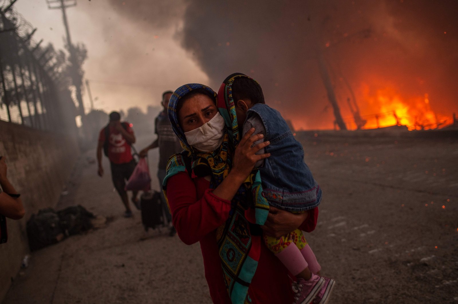 A woman carries a child past flames after a major fire broke out in the Moria migrants camp on the Aegean island of Lesbos, Greece, Sept. 9, 2020. (AFP Photo)