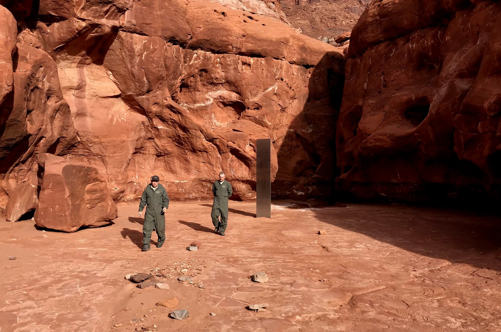 Utah state workers walk near a metal monolith in the ground in a remote area of red rock in the U.S. state of Utah, Nov. 18, 2020. (Utah Department of Public Safety via AP)