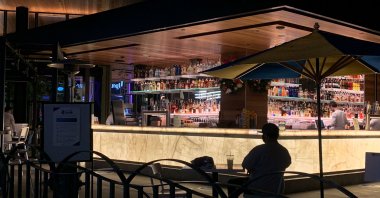 A man sits alone with his drink near the bar as people visit Disneyland where parts of the park opened for more retail and dining as an extension of the Downtown Disney District in Anaheim, California, Nov. 19, 2020. (AFP Photo)