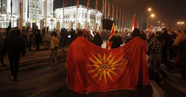 Two men hold an old national flag as opposition supporters gather to protest the government's policy toward Bulgaria, in front of the government building, Skopje, North Macedonia, Nov. 26, 2020. (AP Photo)