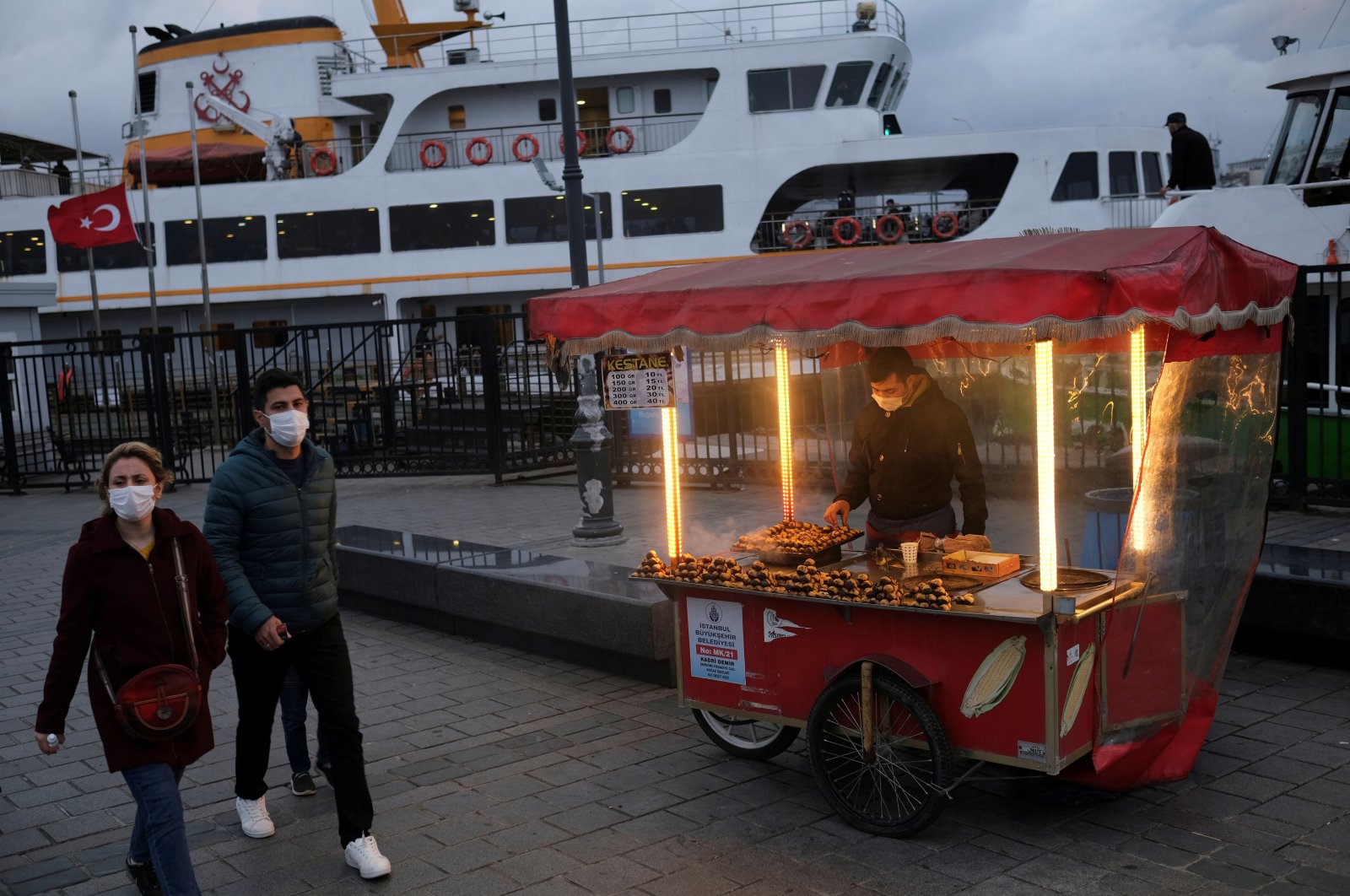 People wearing protective masks walk past a street vendor selling roasted chestnuts in Istanbul, Turkey, Nov. 10, 2020. (Reuters Photo)