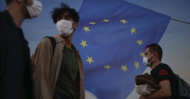 Backdropped by a poster with a European Union flag, people, wearing masks to help protect against the spread of coronavirus, walk in Istanbul, Friday, Oct. 2, 2020. (AP Photo)