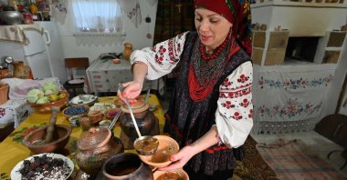An Ukrainian ethnologist and historian, who studies borscht and has 365 of its unique recipes from all over Ukraine in her private collection, wears Ukraine's traditional clothes and headdress cooks borscht in clay pots in the wood stove in the village of Opishnya in Poltava region, Nov. 26, 2020. (AFP Photo)