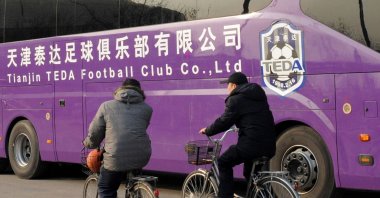 Two men ride past a Tianjin TEDA football club bus on a road in Tianjin, China, Feb. 19, 2013. (AFP Photo)