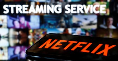A smartphone with the Netflix logo lies in front of displayed "Streaming service" words in this illustration taken on March 24, 2020. (Reuters Photo)