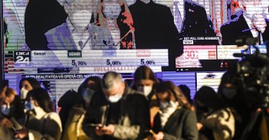 Journalists look at their mobile phones backdropped by large screens showing exit polls in parliamentary elections at the headquarters of the ruling National Liberal Party, in Bucharest, Romania, Dec. 6, 2020. (AP Photo)