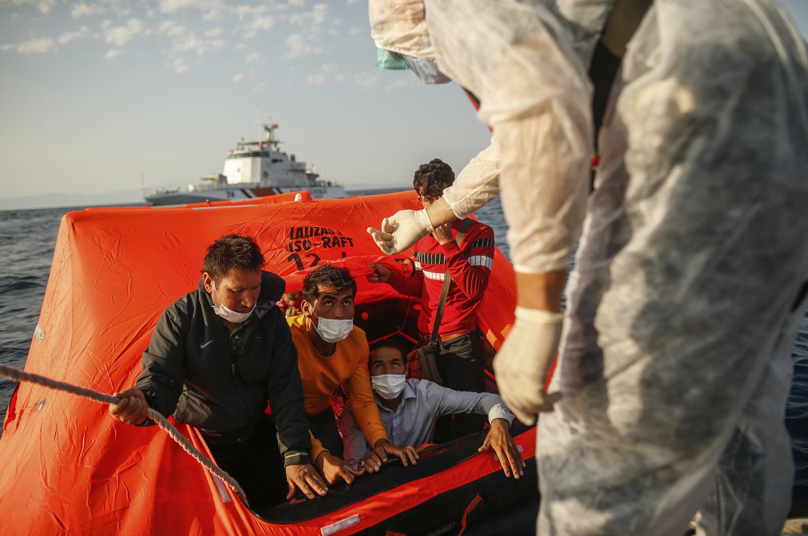 Turkish Coast Guard Command officers on their vessel, wearing protective gear to help prevent the spread of the coronavirus, talk to migrants on a life raft during a rescue operation in the Aegean Sea, between Turkey and Greece, Sept. 12, 2020. (AP File Photo)