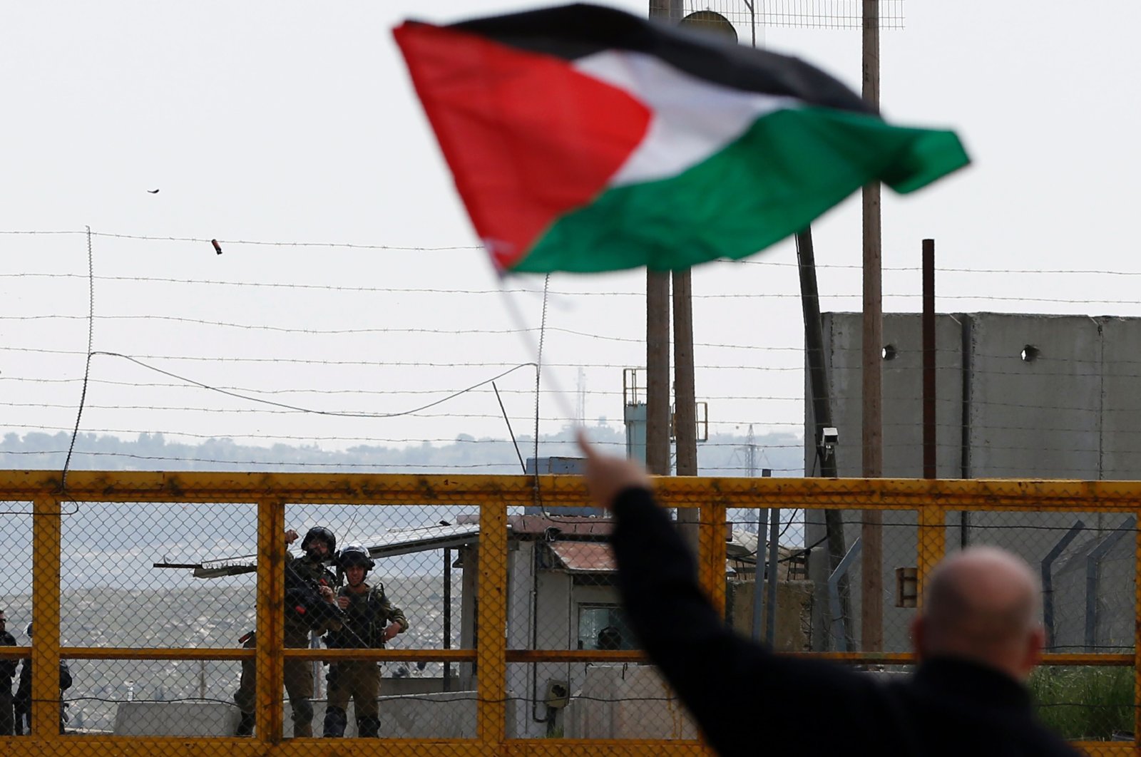 A Palestinian protester waves his national flag in front of Israeli security forces outside the compound of the Israeli-run Ofer prison near Betunia in the Israeli occupied West Bank, March 30, 2016. (AFP Photo)