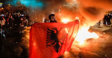 A man holds the Albanian flag as people take part in a demonstration in reaction to the death of Klodian Rasha, after he was shot dead during the country's overnight curfew, in Tirana, Albania, Dec. 10, 2020. (Reuters Photo)