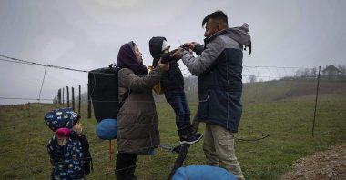 Malika, 2nd left, passes their 5 years old daughter to her husband Mohammed as the Afghan family climb over a wire fence close to the Bosnian-Croatian border near Velika Kladusa in Bosnia-Herzegovina, Dec. 9. 2020. (AP Photo)