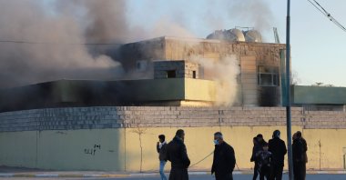 People stand outside a local police station set on fire by protesters in the town of Takia, about 60 kilometers southwest of the city of Sulaimaniyah, on Dec. 8, 2020. (AFP Photo)