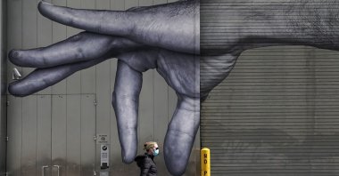 A woman in a mask walks past a mural of a hand on the side of a building in Midtown New York City, Apr. 22, 2020. (AFP PHOTO)