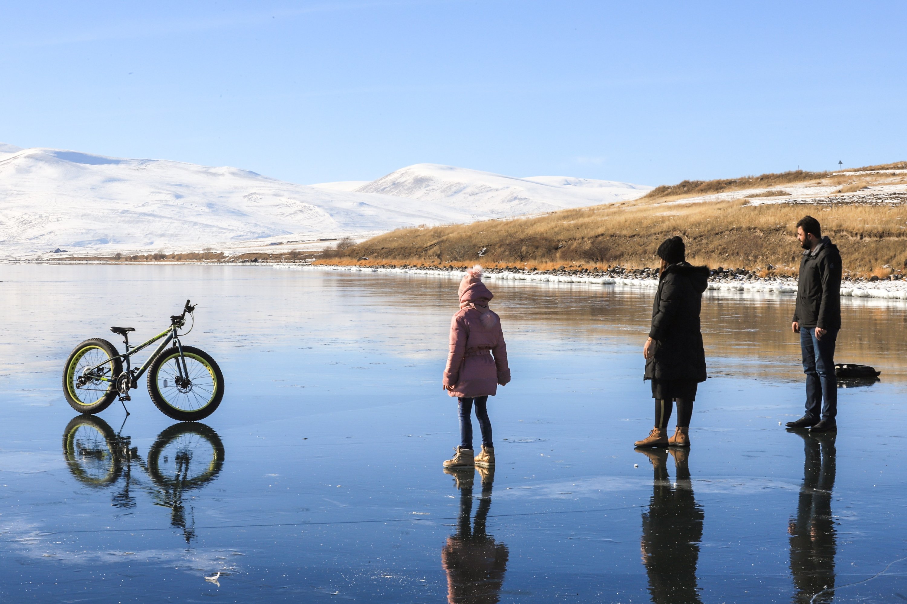 People stand next to a bicycle on the glassy surface of Lake Çıldır in the Çıldır district of Ardahan province, eastern Turkey, Dec. 28, 2020. (IHA Photo)