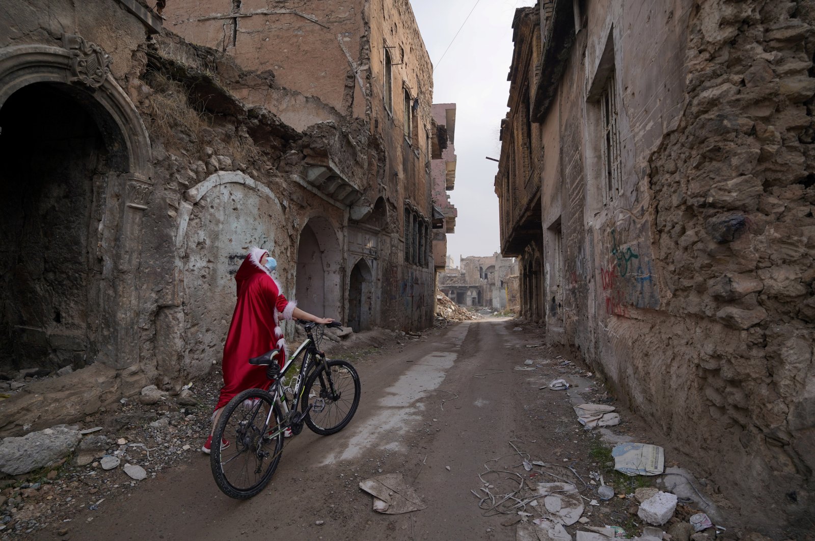 An Iraqi woman, dressed as Santa Claus, looks at the destroyed buildings as she walks with her bicycle in the old city of Mosul, Iraq, Dec. 18, 2020. (Reuters Photo)