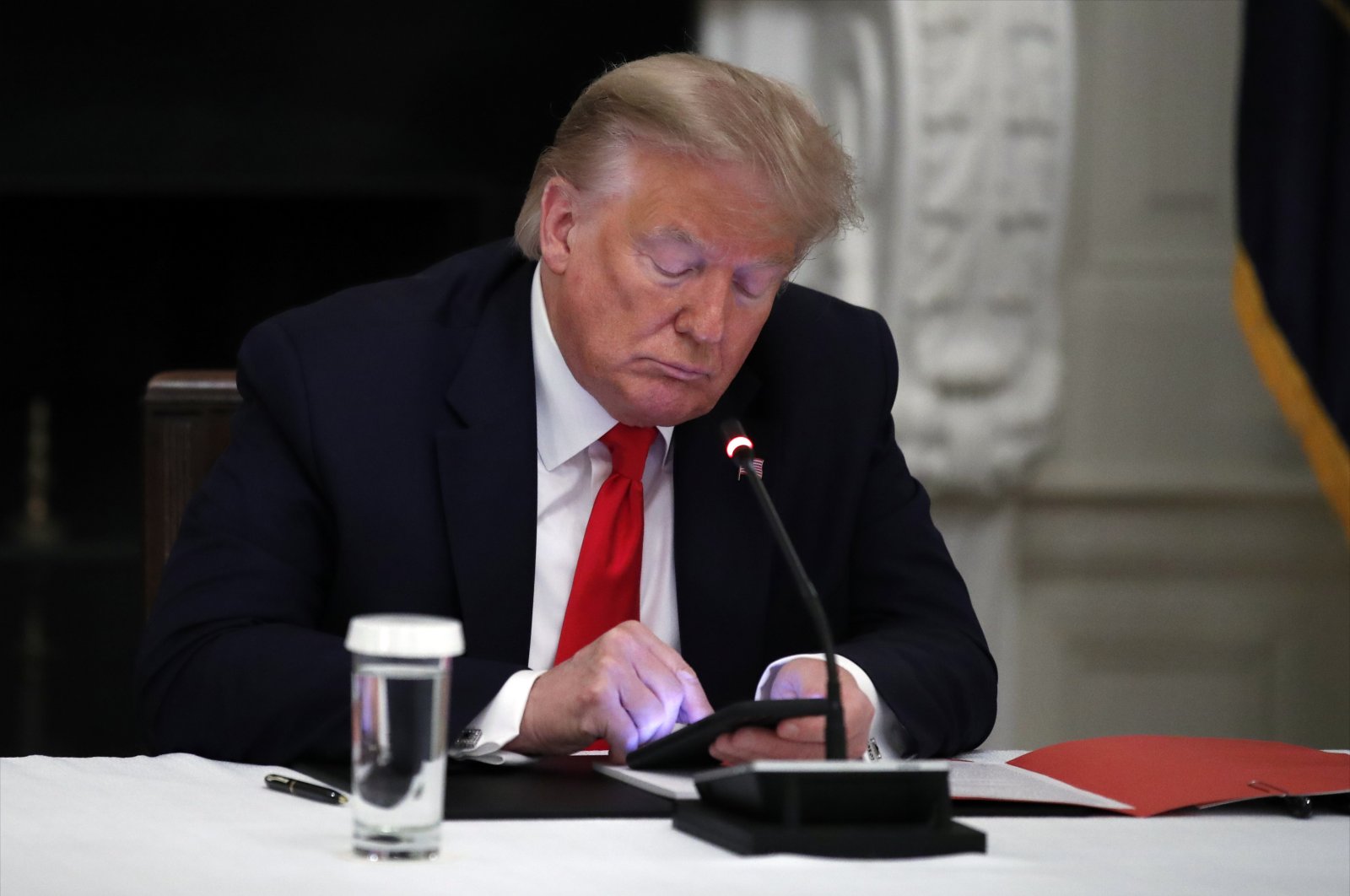U.S. President Donald Trump looks at his phone during a roundtable with governors on the reopening of America's small businesses, in the State Dining Room of the White House in Washington, D.C., June 18, 2020. (AP Photo)