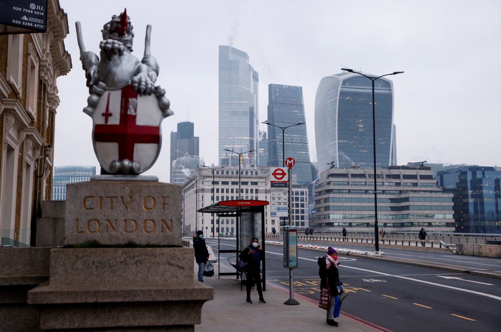 People wearing face masks wait at a bus stop on London Bridge, amid the outbreak of the coronavirus disease (COVID-19), with the City of London financial district in the background, Britain, Jan. 8, 2021. (Reuters Photo)