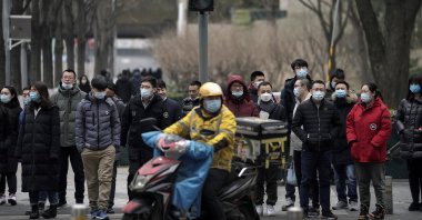 A food delivery worker and office workers wearing face masks to protect themselves from the coronavirus wait to cross a street in Beijing, China, Jan. 14, 2021. (AP Photo)