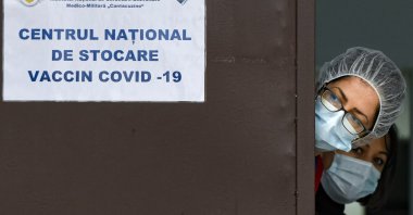 Medical staff peer from behind a door at the National Center for Storage of the COVID-19 Vaccine in Bucharest, Romania on Dec. 18, 2020. (AP Photo)